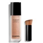 Chanel Les Beiges Water-Fresh Tint clear bottle showcasing the encapsulated pigment droplets inside, sitting elegantly next to its signature small black blending brush, available on glamit.pk Pakistan