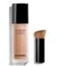 Chanel Les Beiges Water-Fresh Tint clear bottle showcasing the encapsulated pigment droplets inside, sitting elegantly next to its signature small black blending brush, available on glamit.pk Pakistan