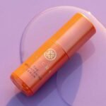 Front view of the luxury orange Tatcha Brightening Face Serum bottle with elegant gold accents, displayed on a clean reflective vanity backdrop, available on glamit.pk Pakistan.