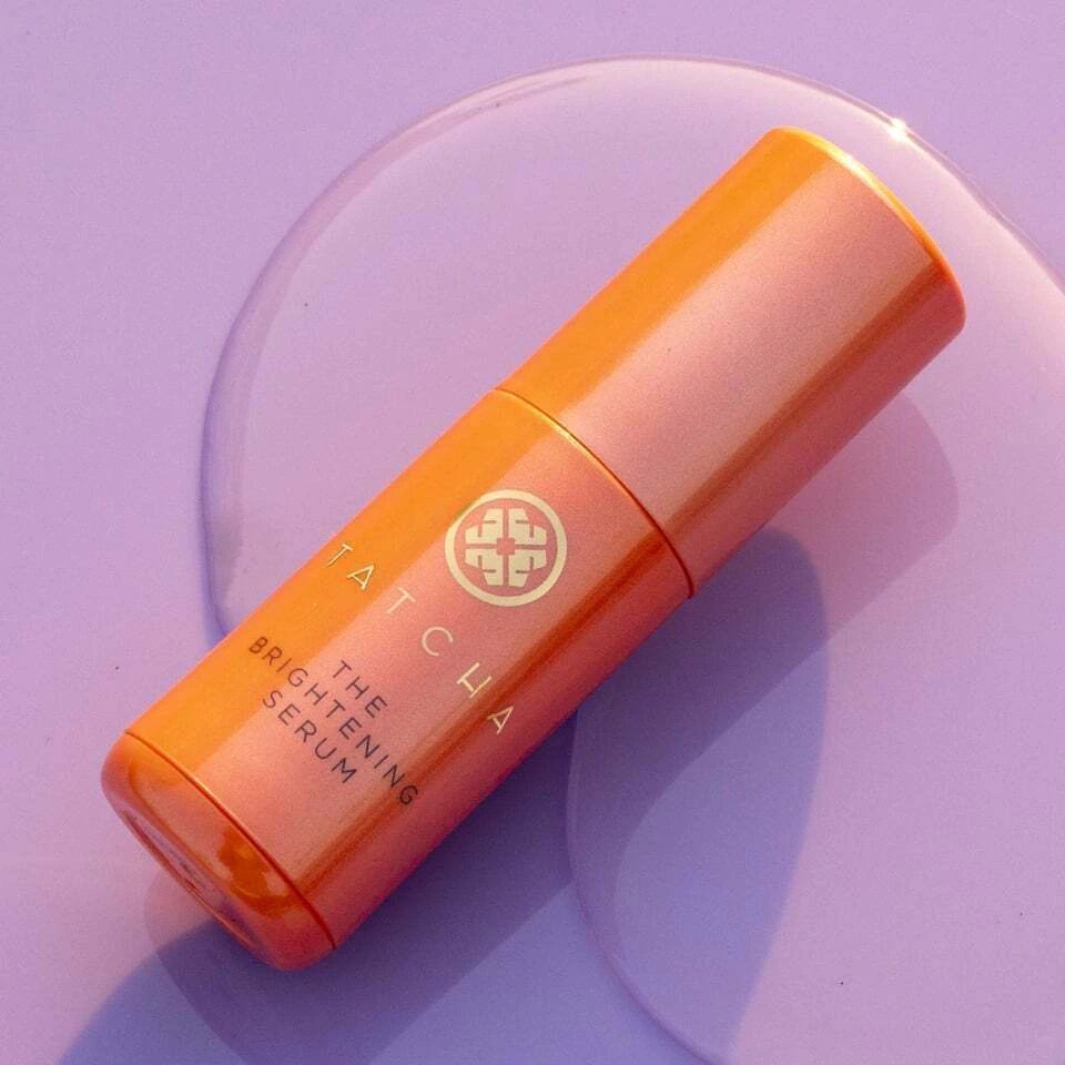 Front view of the luxury orange Tatcha Brightening Face Serum bottle with elegant gold accents, displayed on a clean reflective vanity backdrop, available on glamit.pk Pakistan.